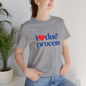 May include: A grey t-shirt with the words "i ❤️ due process" printed in blue with a red heart. The shirt has short sleeves and a crew neck.