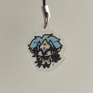 Op de afbeelding: Een heldere, bloemvormige acryl bedel met een stripfiguur met blauw haar en een zwart-witte outfit. De bedel hangt aan een zwart koord dat is bevestigd aan een zilverkleurige metalen sluiting.