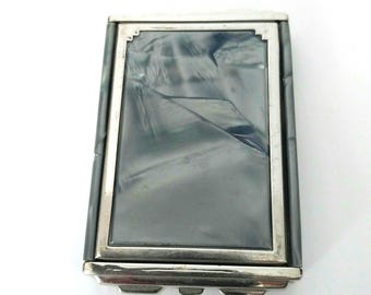 Könnte beinhalten: Ein rechteckiges, vintage Kompakt-Etui mit silberfarbenem Metallrahmen. Die Mitte zeigt ein dunkelgraues, marmoriertes Design. Das Kompakt-Etui hat eine Klappöffnung und einen dekorativen unteren Rand.