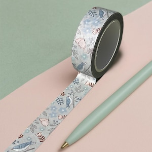 Könnte beinhalten: Dekoratives Washi-Tape mit einem Muster aus Vögeln, Blumen und Blättern auf hellblauem Hintergrund. Ein hellgrüner Stift liegt neben der Rolle. Der Hintergrund ist rosa und grün.