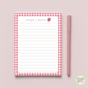 Puede incluir: Un bloc de notas rayado con un borde de cuadros rojos y blancos. El bloc de notas tiene el texto "Steph's Notes" y un gráfico de fresa. Un bolígrafo rosa descansa junto al bloc de notas. El bloc de notas está diseñado para tomar notas.