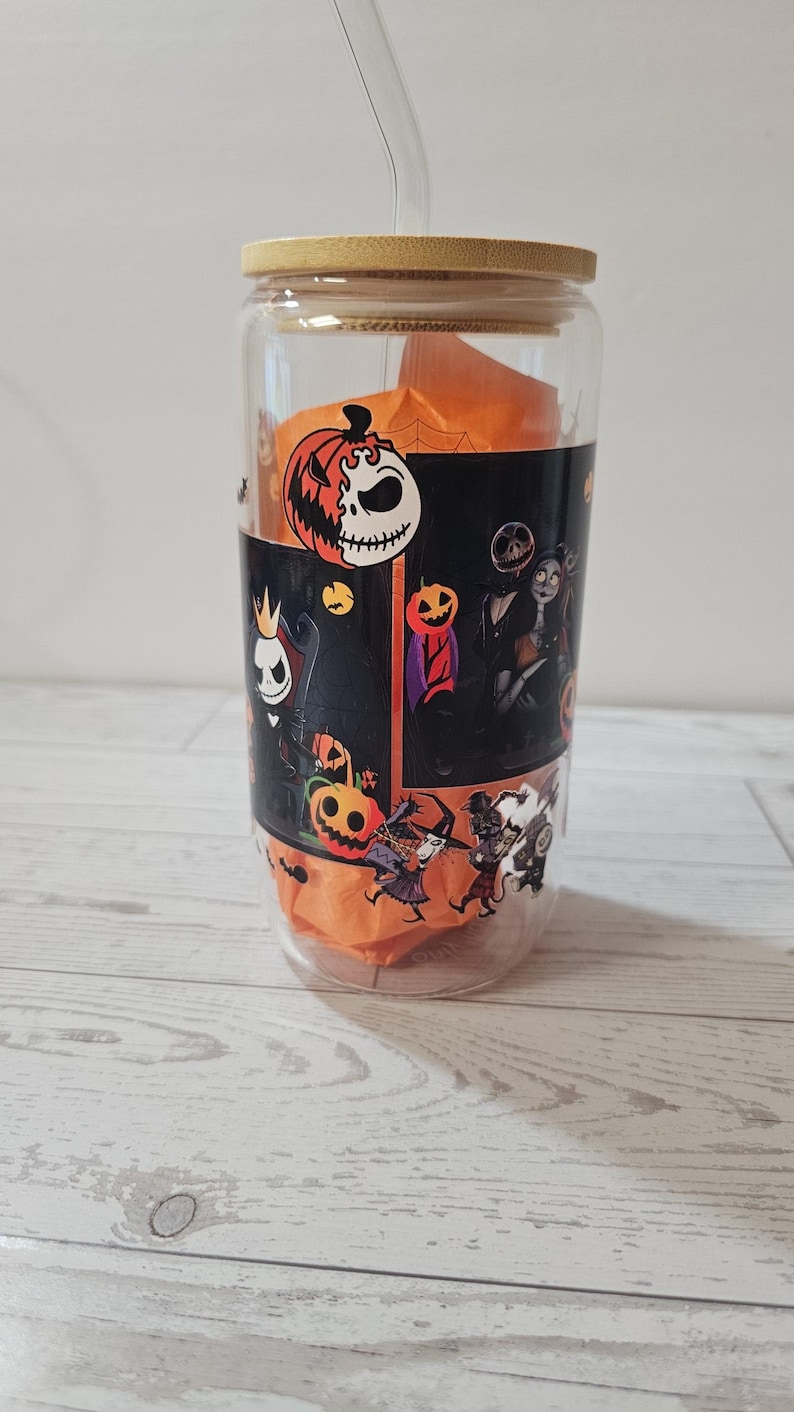 Puede incluir: Un vaso de vidrio transparente con tapa de bamb&uacute; y pajita. El vaso presenta un dise&ntilde;o envolvente con personajes e im&aacute;genes de Pesadilla antes de Navidad, incluyendo a Jack Skellington y calabazas. El vaso contiene papel de seda naranja.