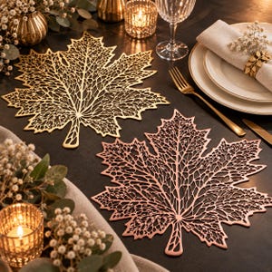 May include: Two decorative placemats shaped like maple leaves, one in a metallic gold finish and one in a metallic rose gold finish. Both placemats feature an intricate, laser-cut filigree pattern that mimics the veins of a natural leaf.