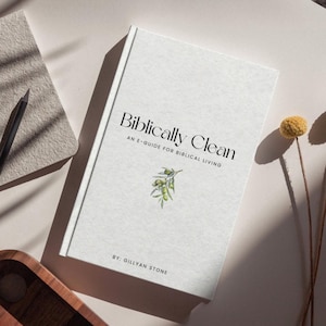May include: A white book titled "Biblically Clean" with the subtitle "An E-Guide for Biblical Living." The cover features a sprig of green olives and the author's name, Gillyan Stone. A pencil and notepad are visible in the background.