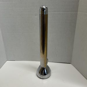 May include: A vintage flashlight with a chrome and gold-toned metal body. The flashlight has a ribbed cylindrical shaft, a bulbous base, and a rounded top. It features a small switch on the side.