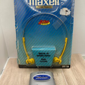 May include: A pair of yellow Maxell lightweight stereo head buds in original blue and yellow packaging with the text Lightweight Stereo Head Buds, Action Sports, and Ideal for all portable stereos. A silver Sony Walkman radio is positioned in front.