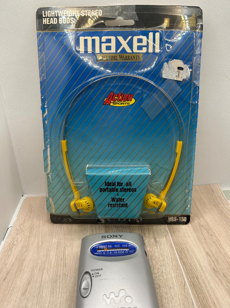 May include: A pair of yellow Maxell lightweight stereo head buds in original blue and yellow packaging with the text Lightweight Stereo Head Buds, Action Sports, and Ideal for all portable stereos. A silver Sony Walkman radio is positioned in front.