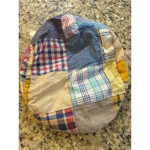 May include: A patchwork newsboy cap featuring a variety of fabrics in shades of blue, red, yellow, and tan. The cap has a rounded crown and a small, stiff brim. The fabric is pieced together in a patchwork design.