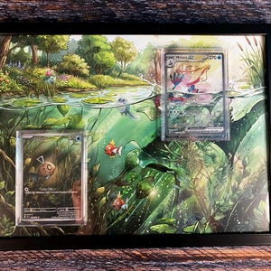Könnte beinhalten: Gerahmtes Kunstwerk mit einer ruhigen Wasserlandschaft und zwei Pokémon-Sammelkarten. Das Kunstwerk zeigt einen Teich mit Fischen und Seerosen. Die Karten sind in Schutzhüllen, die eine Feebas- und eine Milotic V-Karte zeigen.