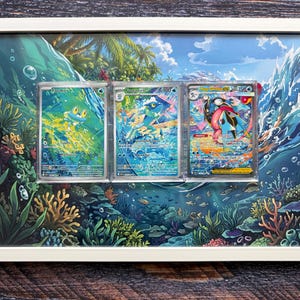 Könnte beinhalten: Ein weißer rechteckiger Rahmen mit drei Pokémon-Sammelkarten vor einem lebendigen Unterwasserhintergrund. Die Karten zeigen Froakie, Frogadier und Greninja EX, jeweils in einer transparenten Schutzhülle innerhalb des Rahmens.