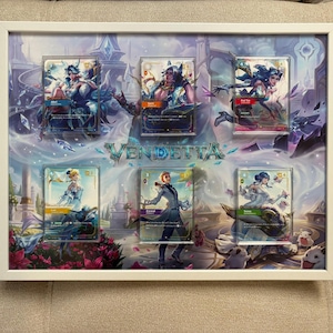 May include: A white rectangular frame containing a display of six collectible trading cards arranged over a fantasy-themed background with the word VENDETTA printed in the center. The cards feature various illustrated characters in colorful attire.