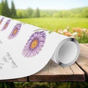 Może przedstawiać: Zwinięty biały papier z akwarelowymi ilustracjami fioletowych kwiatów astrów z żółtymi środkami i zielonymi liśćmi. Widoczny jest tekst "Aster - Wisdom that blooms". Tło przedstawia rozmyty plener.
