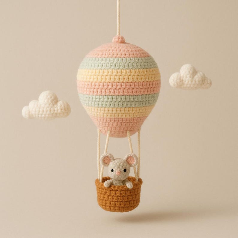 Puede incluir: Un globo aerost&aacute;tico de ganchillo en colores pastel, con un peque&ntilde;o rat&oacute;n en una cesta marr&oacute;n. El globo est&aacute; rayado en rosa, amarillo y verde menta. Dos nubes blancas de ganchillo. Decoraci&oacute;n de guarder&iacute;a.