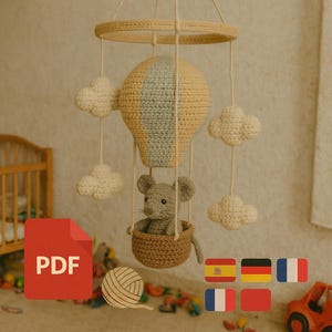 Puede incluir: M&oacute;vil de beb&eacute; hecho a mano con ganchillo, con un dise&ntilde;o de globo aerost&aacute;tico amarillo y gris, y un peque&ntilde;o rat&oacute;n gris en una cesta. El m&oacute;vil incluye acentos de nubes blancas y est&aacute; suspendido de un marco circular. Un icono PDF es visible.