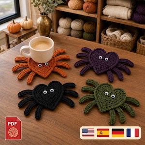 Pode incluir: Quatro porta-copos de crochê em formato de coração e aranha nas cores laranja, roxo, preto e verde-oliva. Cada porta-copos tem oito pernas e dois olhos móveis. Uma caneca de cerâmica bege com café está sobre a aranha laranja em madeira.