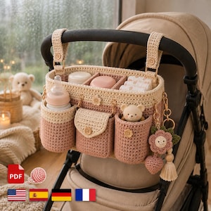 May include: A beige and dusty rose crochet stroller organizer featuring multiple compartments, a bottle holder, a small flap pocket, and a hanging flower charm. The organizer is attached to the handlebar of a beige stroller with two crochet straps.