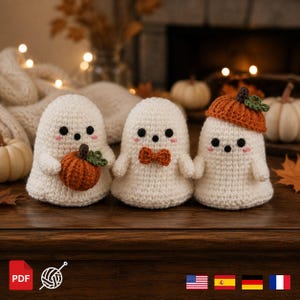 May include: Three crocheted ghost figures in off-white yarn with black bead eyes and pink stitched cheeks. The first ghost holds a small orange pumpkin, the second wears an orange bow tie, and the third wears an orange pumpkin-shaped hat.