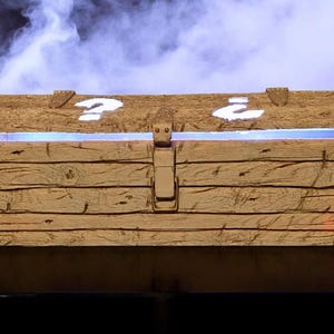 Könnte beinhalten: Eine hölzerne Schatzkiste mit einem Klappdeckel und einem Metallverschluss. Der Deckel zeigt zwei weiße Fragezeichen. Das Innere leuchtet mit blauem Licht. Die Truhe hat ein rustikales, gealtertes Aussehen.