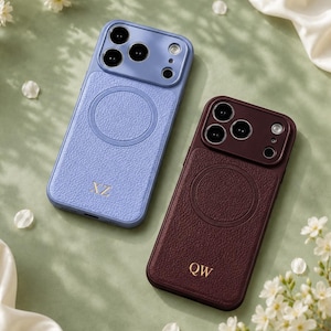 Puede incluir: Dos fundas de teléfono rectangulares con un acabado de textura similar al cuero, una en azul claro y otra en granate oscuro. Cada funda presenta un anillo magnético circular, un recorte para la cámara e iniciales doradas, XZ en la azul y QW en la granate.