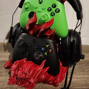 May include: A gaming setup featuring two Xbox controllers, one green and one black, with a black headset. The controllers are adorned with red, flame-like accents. The headset has a microphone.