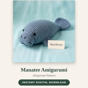 Könnte beinhalten: Ein blaues gehäkeltes Manati-Amigurumi-Spielzeug mit schwarzen Sicherheitsaugen und gestickten Gesichtsdetails. Eine kleine weiße Karte mit dem Text WasiWorks liegt neben dem Spielzeug. Der Text WasiWorks, Manatee Amigurumi, 15 cm lang ist zu sehen.