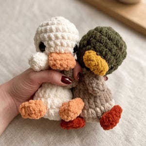 May include: Two crocheted duck toys. One is white with orange feet and beak, the other is green with a yellow beak and orange feet. The ducks are handmade and have black eyes. The toys are soft and cuddly.