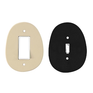 May include: Two oval-shaped light switch covers. One is beige with a white switch, the other is black with a white switch. Both have a single toggle switch and two screw holes.