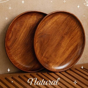 Könnte beinhalten: Zwei runde Teller aus natürlichem Akazienholz in einem warmen Braunton. Die Teller werden auf einer Holzoberfläche präsentiert, mit dem Text "Natural Acacia Wood Plates" in dekorativer Schrift.