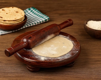 Puede incluir: Un rodillo de madera descansa sobre una tabla redonda de madera con un círculo de masa aplanada. Una pila de panes planos se encuentra en un cuenco de madera, y un cuenco pequeño de harina está cerca.