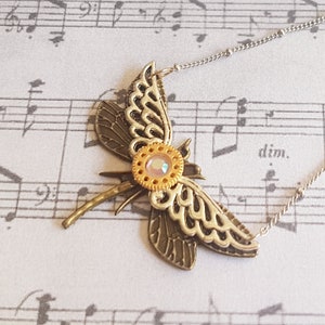 May include: A silver chain necklace with a dragonfly pendant. The dragonfly is made of metal and has a gold and silver finish. The dragonfly has a clear iridescent stone in the center of its body.