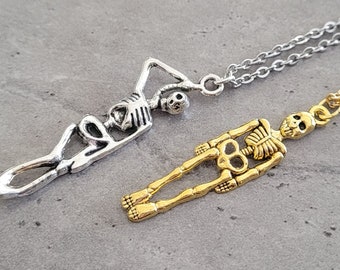 May include: Two skeleton necklaces, one silver and one gold, on a gray textured surface.
