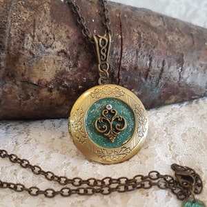 May include: A gold locket necklace with a green glitter and floral design. The locket has a small rhinestone in the center. The necklace has a bronze chain and a tag that says "Made with Love".