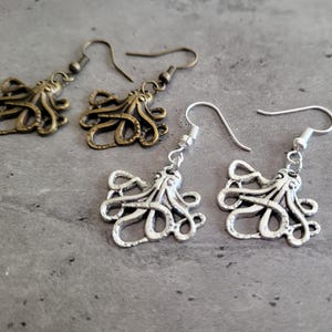 Peut inclure: Une paire de boucles d'oreilles en forme de pieuvre, l'une en argent et l'autre en bronze. Les boucles d'oreilles sont en métal et présentent un design détaillé.