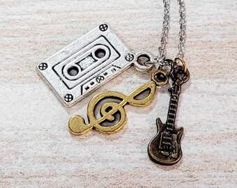 May include: Silver chain necklace with three charms: a silver cassette tape, a gold treble clef, and a bronze electric guitar.