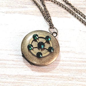May include: A bronze locket necklace with a circular pendant featuring a gear design and six green gemstones.