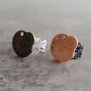 May include: Two steampunk-style rings with clock face and gear designs. One ring has a white metal band and the other has a black metal band.