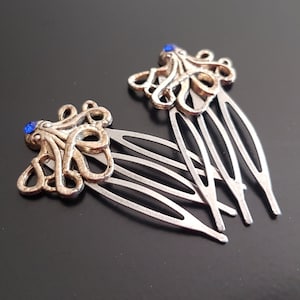 Op de afbeelding: Twee zilveren haar kammen met gouden octopus ontwerpen en blauwe strass steentjes.