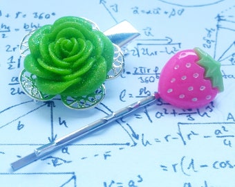 May include: Two hair clips, one with a green glitter rose and the other with a pink glitter strawberry. Both clips are on a white background with blue ink.