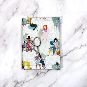 May include: Silver-handled embroidery scissors on a fabric case. The case has a whimsical print of people with cats in a light blue floral pattern. The scissors have a decorative design on the handles.