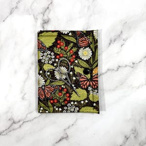 May include: A small green fabric pouch with a floral and butterfly print. The pouch has a black button closure and contains a pair of small silver scissors.
