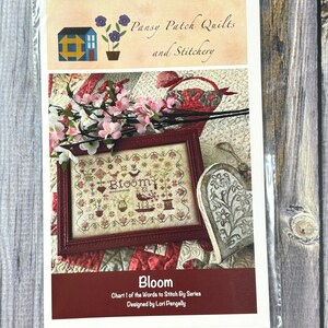May include: A cross stitch pattern for a floral design with the word "Bloom" in the centre. The pattern is titled "Bloom" and is part of the "Words to Stitch By" series. It was designed by Lori Pengelly.