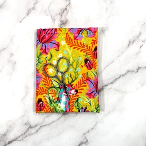 May include: A yellow fabric scissor case with a colourful floral and deer design. The case holds a pair of silver embroidery scissors. The design includes red, pink, and green flowers and foliage.