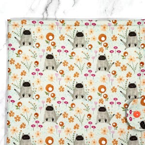 May include: A rectangular fabric mat featuring a repeating pattern of Siamese cats and small orange and pink flowers on a light mint green background. The mat includes a small, rounded corner flap secured with a bright orange circular snap button.