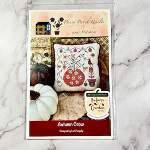 Peut inclure: Un modèle de point de croix pour un coussin représentant une scène d'automne avec une citrouille, un arbre et un corbeau. Le modèle est intitulé "Autumn Crow" et est conçu par Lori Pengelly. Le modèle est de Cottage Garden Threads et fait partie de la "Palette de jardin d'automne".