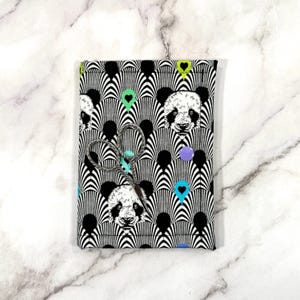 May include: A fabric pouch featuring a panda bear design in black and white, with colourful heart and dot accents. The pouch is tied with twine and small scissors. The background is a white marble surface.