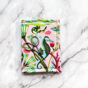 May include: A rectangular fabric case featuring a light pink background with a colourful pattern of green seahorses, teal aquatic plants, and red coral. A pair of silver metal embroidery scissors with a twisted handle rests on the case.