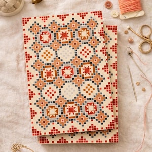 May include: Two rectangular notebooks with a geometric pattern in red, orange, blue, and cream. The notebooks are stacked on top of each other. Sewing notions, including a thimble, thread, and scissors, are scattered around the notebooks.