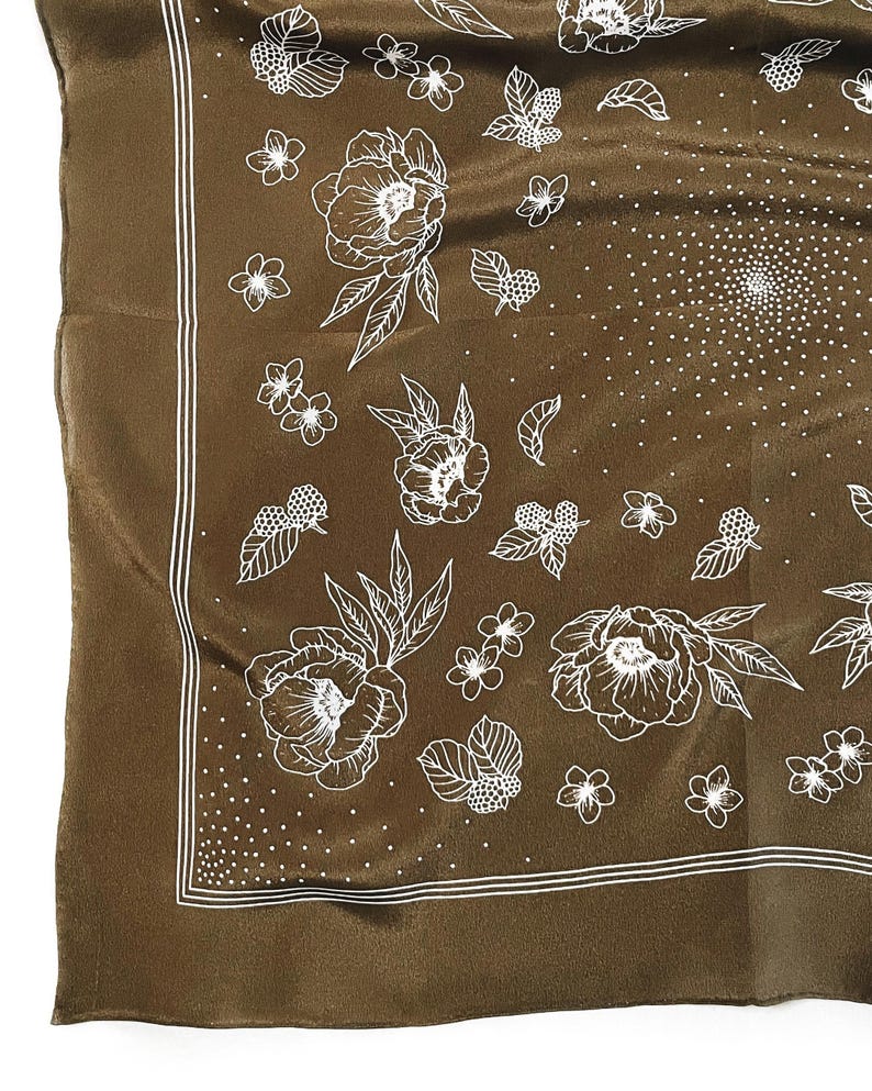 K&ouml;nnte beinhalten: Ein quadratischer, brauner Seidenschal mit wei&szlig;em Blumenmuster. Das Design umfasst gro&szlig;e Bl&uuml;ten, kleine Bl&uuml;ten, Bl&auml;tter und Beeren. Ein wei&szlig;er, doppelt gef&uuml;tterter Rand umrahmt den Rand des Schals, und ein gepunktetes Muster f&uuml;llt die Mitte.