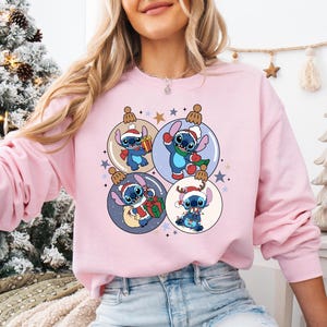 A woman wearing a pink sweatshirt with a Christmas-themed design featuring characters from the Disney animated film Lilo & Stitch.