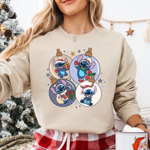 A woman wearing a beige sweater with a Christmas-themed graphic design featuring four cartoon characters from the Disney movie Lilo & Stitch.
